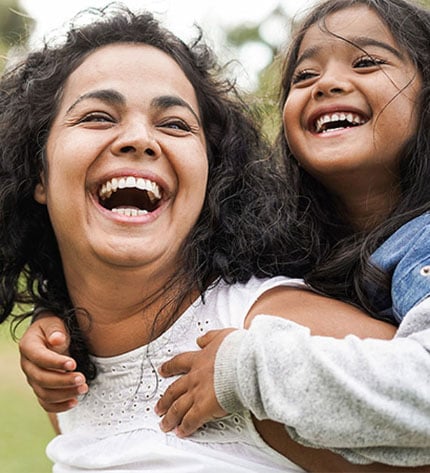 Mulher sorridente num parque com a filha às costas também sorridente