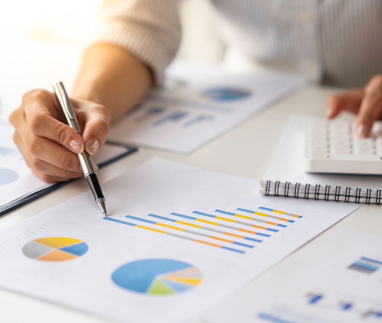 Secretária com documentos com gráficos enquanto uma pessoa escreve à mão num dos documentos