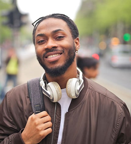 Foto retrato de homem sorridente com headphones à volta do pescoço e mochila ao ombro