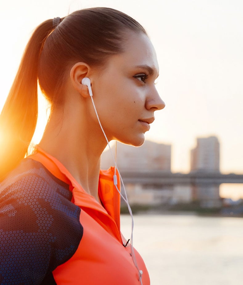 Mulher com roupa de desporto e fones nos ouvidos ao pôr do sol