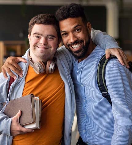 Homem abraçado a rapaz com síndrome de Down com livros na mão