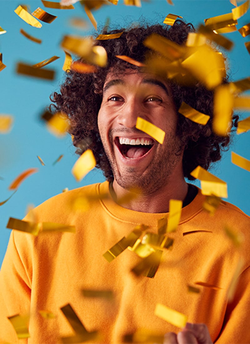 Homem feliz e sorridente com confetis dourados a cair