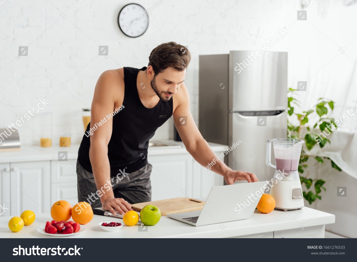 stock-photo-handsome-man-using-laptop-near-blender-with-smoothie-and-fruits-1661276533