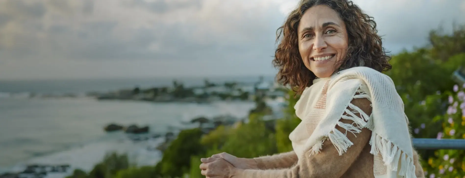 senhora-apoiada-numa-varanda-a-sorrir-com-vista-praia
